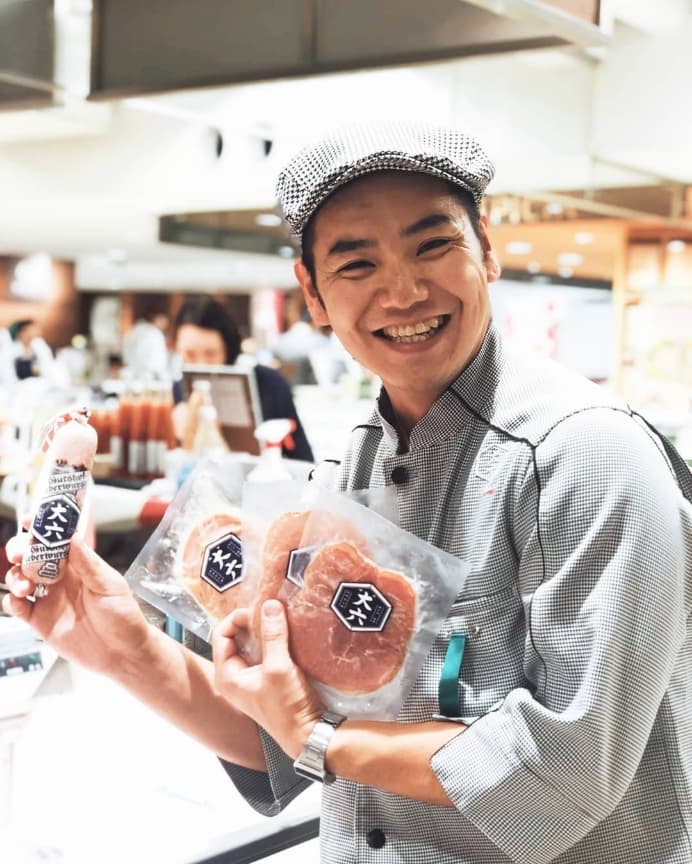 『大六』のロゴが入った田原ポークの商品を手に、満面の笑みを浮かべる店頭スタッフの様子