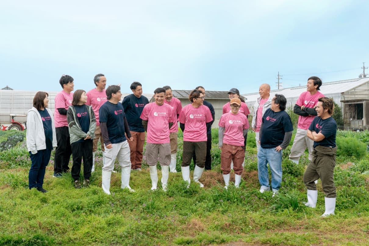 G-FARMのロゴ入りTシャツを着用し、農場内で笑顔で談笑するスタッフ一同の集合写真